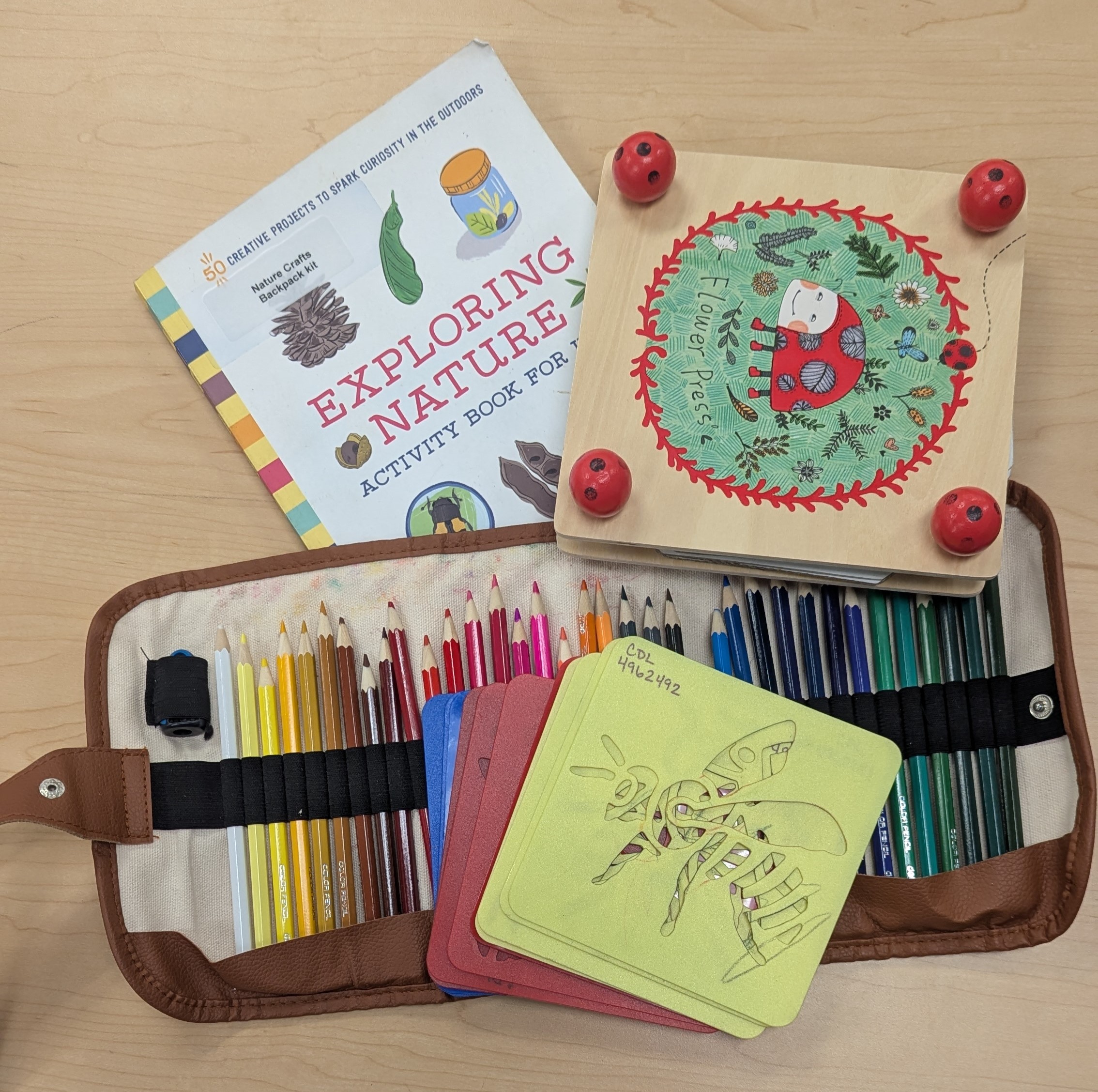 displays contents of nature crafts backpack kit: Flower press, book, stencils, and coloring pencils. 
