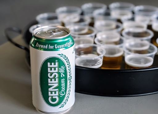 A can of Genesee Cream Ale, in front of a tray full of sample pours, in the Community Room. 