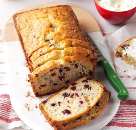 Cranberry almond bread, sliced halfway down the load, on a white plate. 