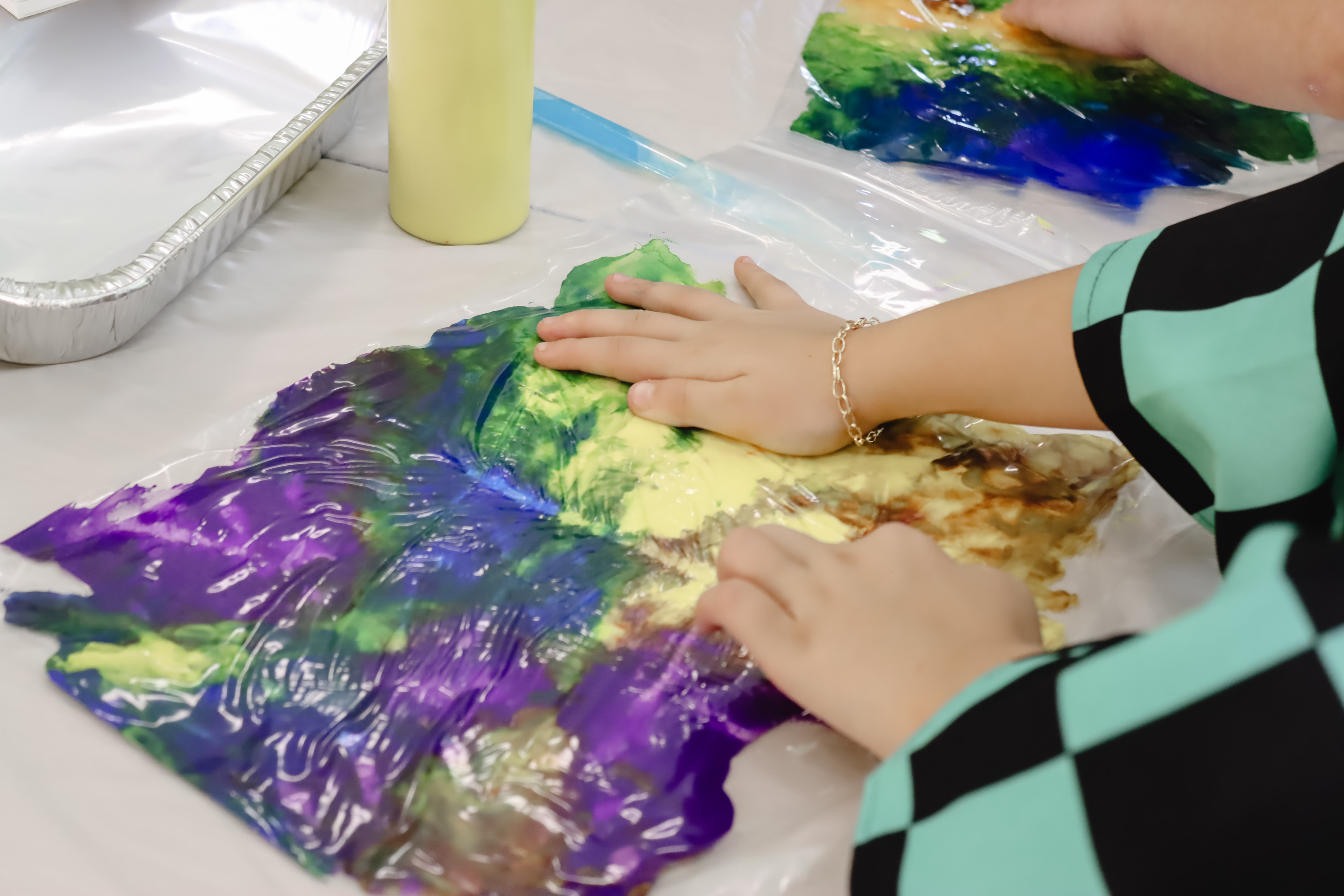 A child's hands pressing into a bag filled with colorful paints, as a sensory activity at the Library. 