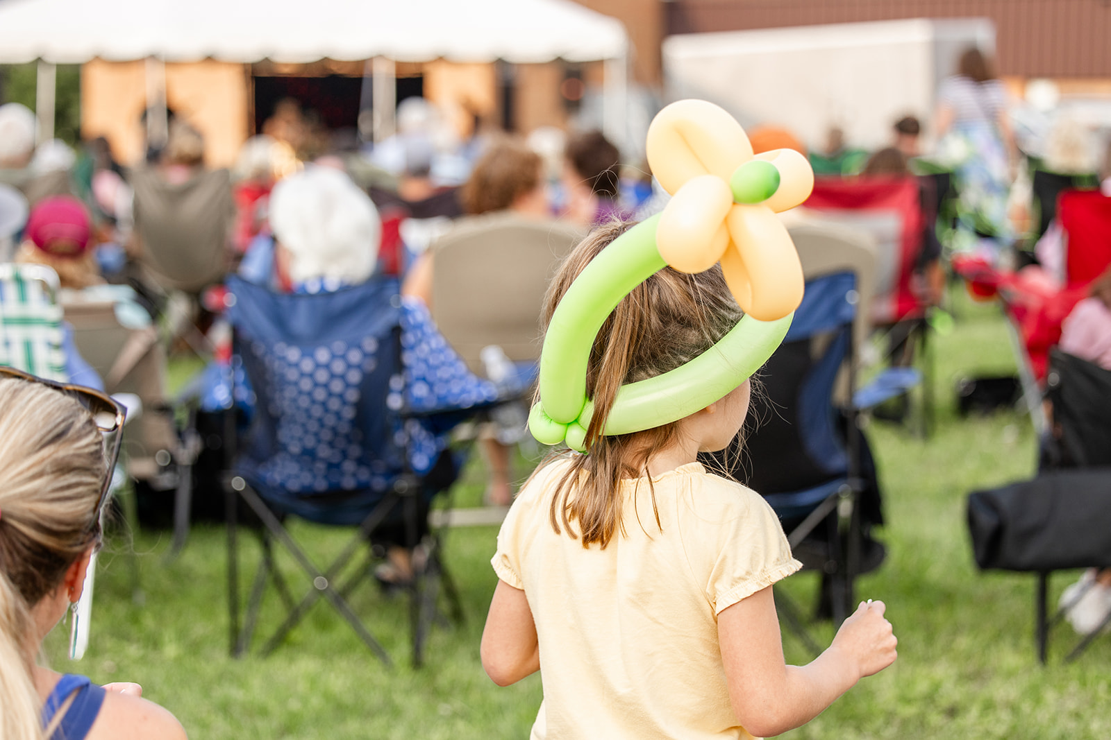A child on the South Lawn wearing a yellow shirt and a green and yellow balloon crown. 