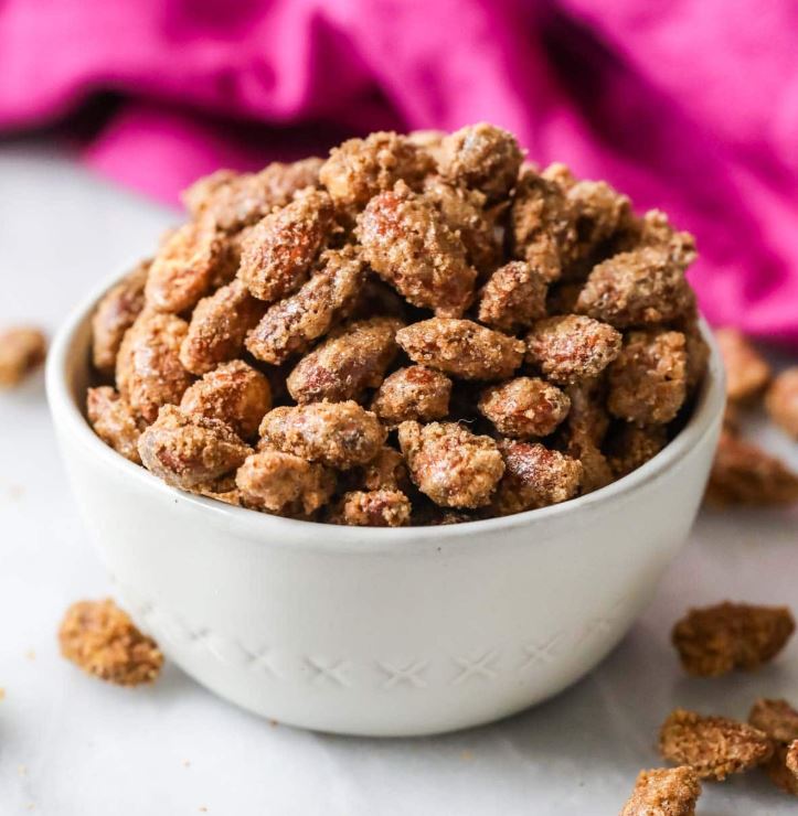 A white ceramic bowl filled with candied almonds, with a pink background. 