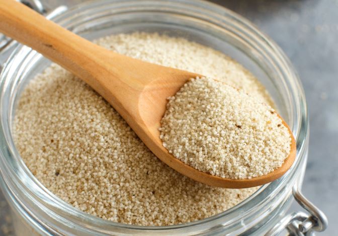 A wooden spoon scoops dry fonio our of a glass jar. 