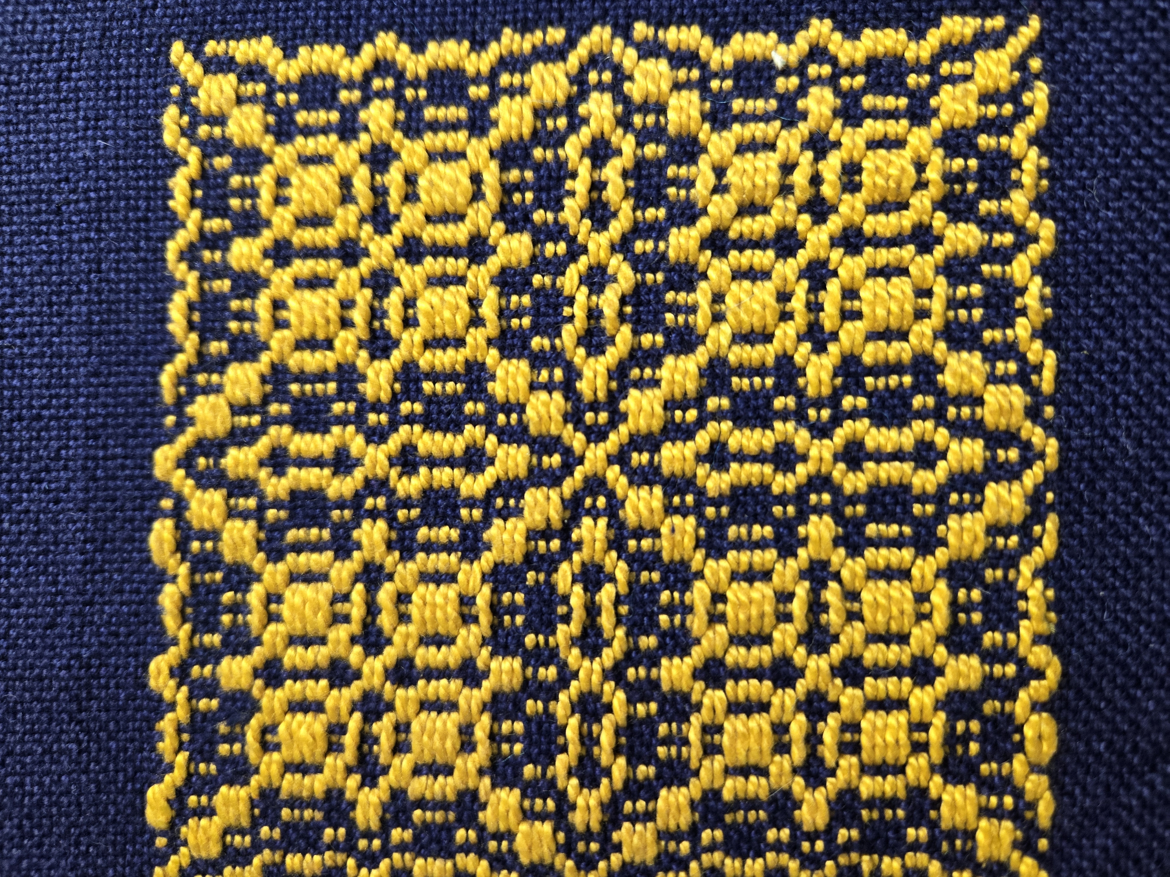 A detail of yellow overshot weaving on a blue woven field.