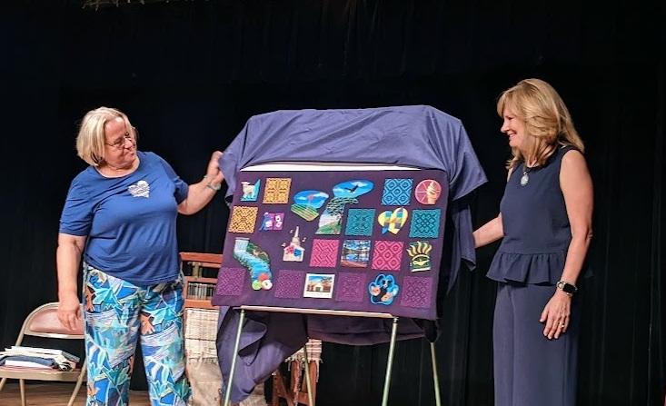Two women are removing the covering off of a textile are piece.