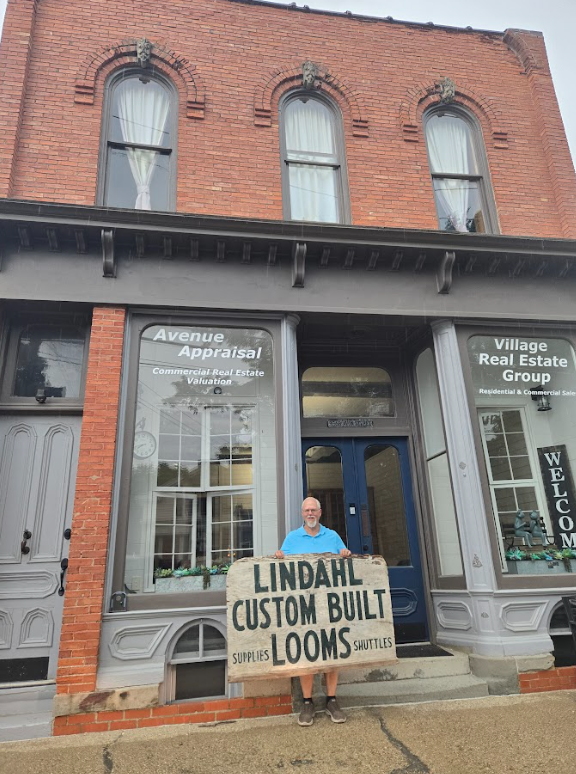 The original Lindahl Looms sign, held by Clifford Lindahl's son in front of the original storefront. 