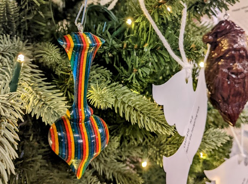 A colorful handmade ornament hanging on the tree, next to various Giving Tree doves. 