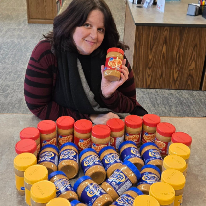 Liz with PB jars on a table, arranged in a heart shape. 