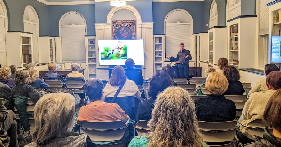 Brian from Bees in the D lecturing about pollinators to a seated audience in the Community Room. 