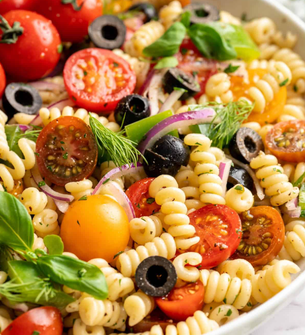 Pasta salad featuring cherry tomatoes, olives, fresh basil, dill, and red onions. 
