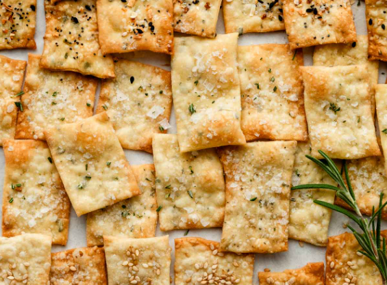 A variety of homemade crackers on a platter, with a sprig of rosemary.