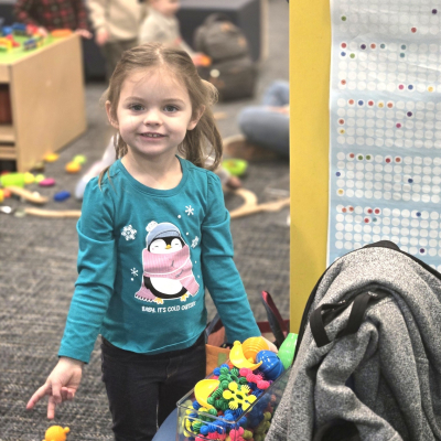 A child posing next to the new sensory/manipulative toys in the Youth department. 