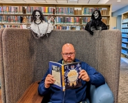 Librarian Erik reading a spooky ghost book, completely unaware that there are two ghosts hovering over his chair. 