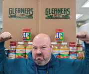 Erik making HUGE muscles in front of two Gleaners boxes, with canned and boxed food alongside. 