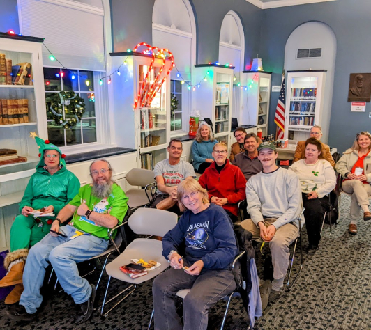 Happy folks sitting in rows of chairs during an Ale Together Now session, in the decorated Community Room.