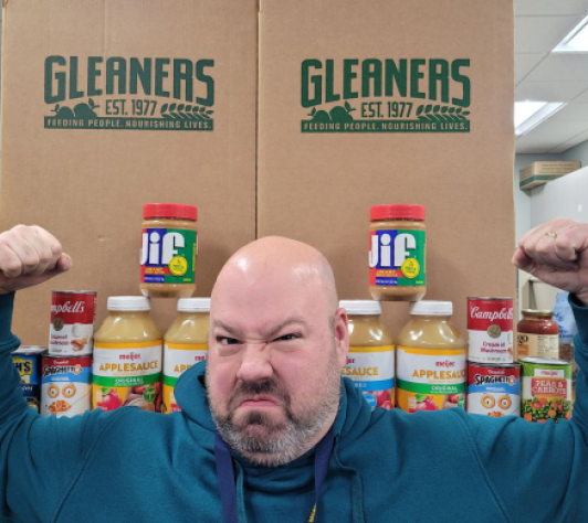 Erik making HUGE muscles in front of two Gleaners boxes, with canned and boxed food alongside. 