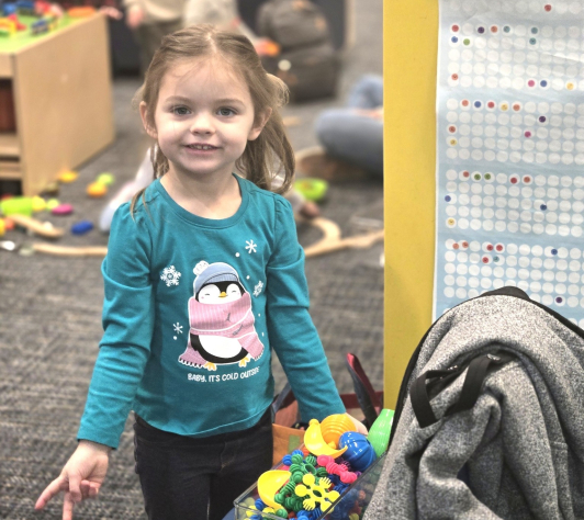 A child posing next to the new sensory/manipulative toys in the Youth department. 