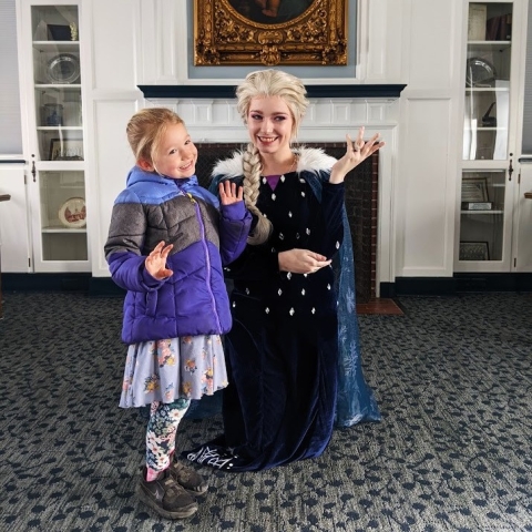 Queen Elsa and a little patron posing together in the Community Room. 