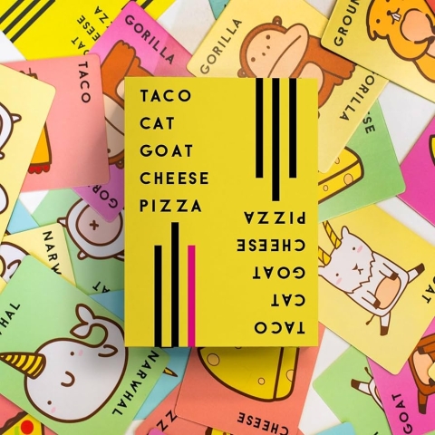 Looking down at the yellow box for Taco Cat Goat Cheese Pizza game, with cards for the game underneath. 