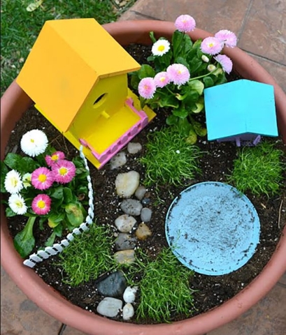 Looking down at a flower pot filled with dirt and topped with a tiny house, pebbles, and other garden items. 