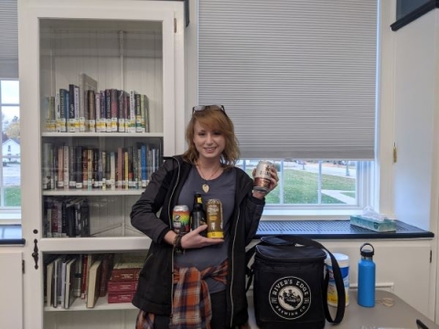 Michelle holding cans and bottles of beer in the Community Room. 
