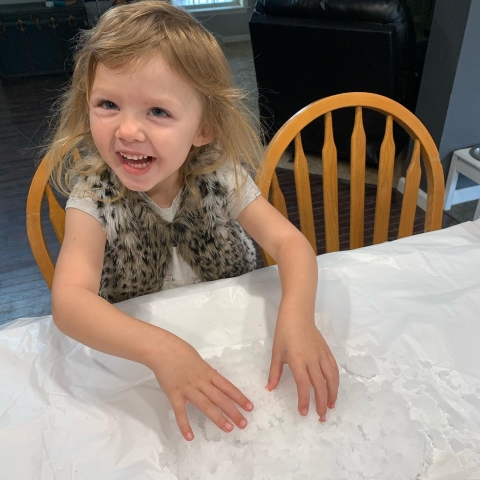 A child seated at a table playing with a sensory snow kit. 