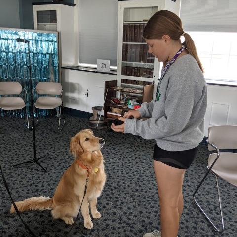 Image of a teen about to give a dog a treat in the Community Room of the Library. 