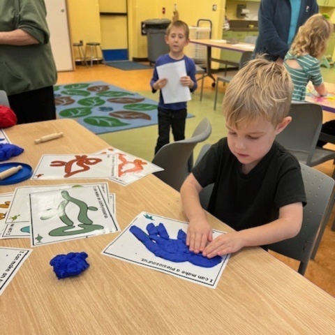 A child seated at a table working on a craft. 
