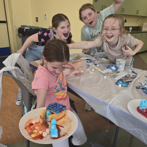 Kids at a table holding up a peep house on a paper plate. 