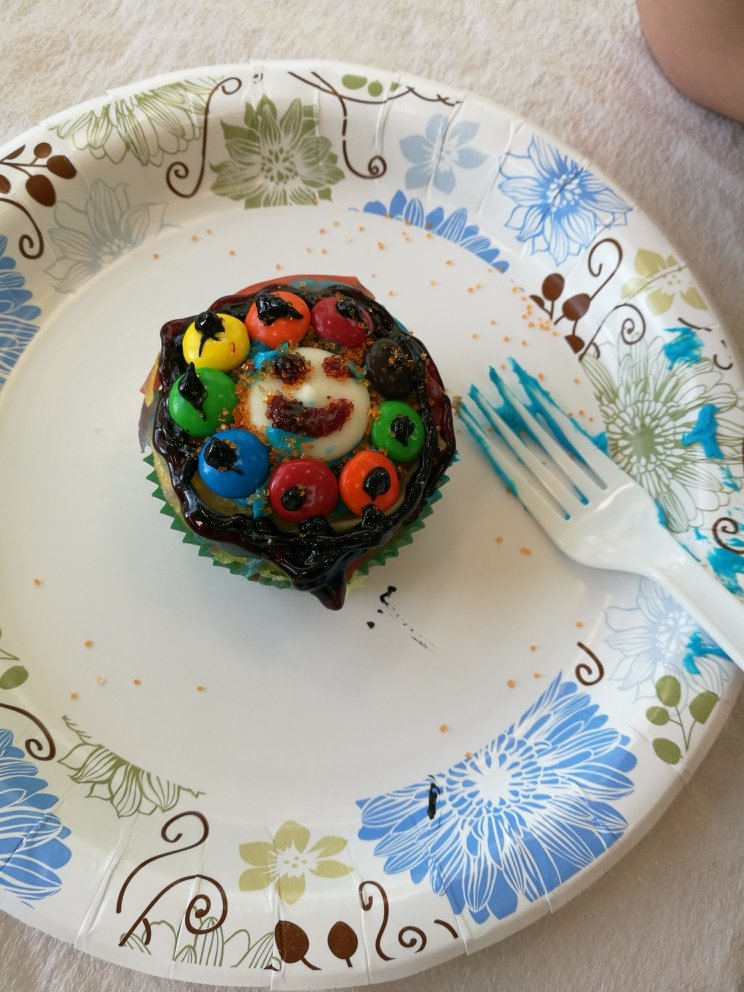 A decorated cupcake with a smiley face and decorated candies. 