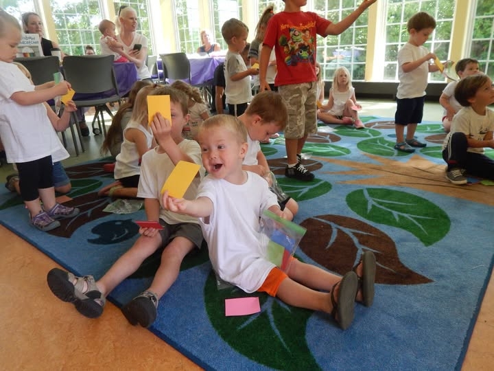Children gathered in the Youth Program Room, holding up yellow cards as a part of a color game. 