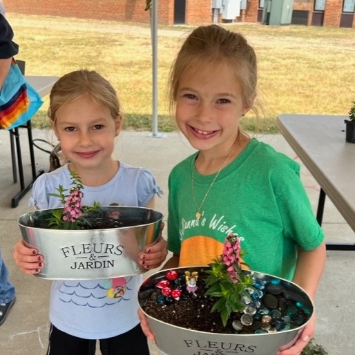 Two kids under the canopy on the South Lawn, holding up handmade fairy gardens. 