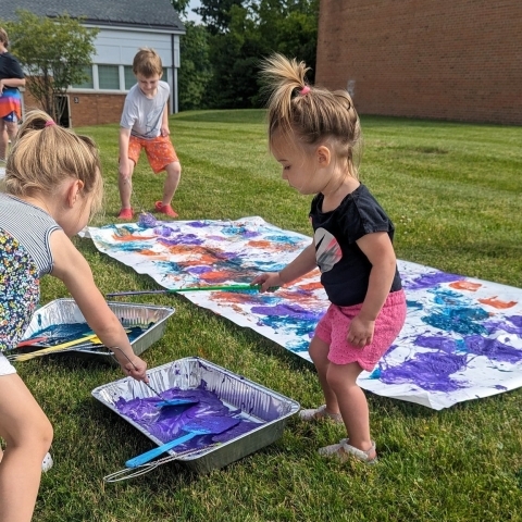 A toddler playing with a variety of paints on the South Lawn. 