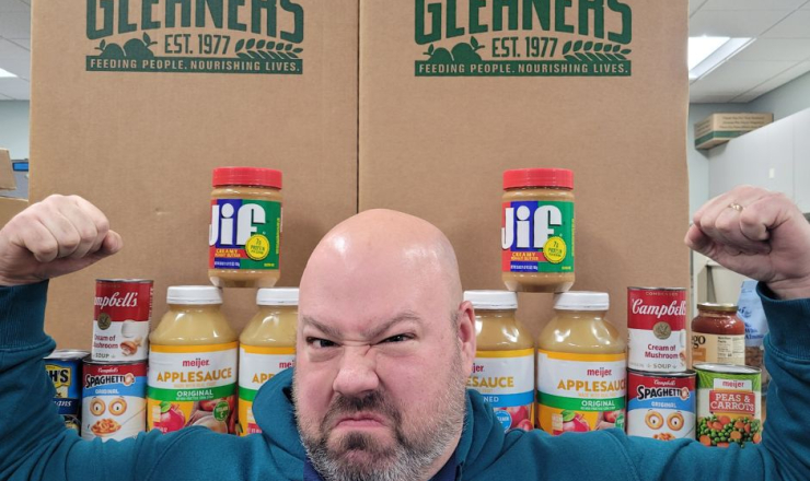 Erik making HUGE muscles in front of two Gleaners boxes, with canned and boxed food alongside. 